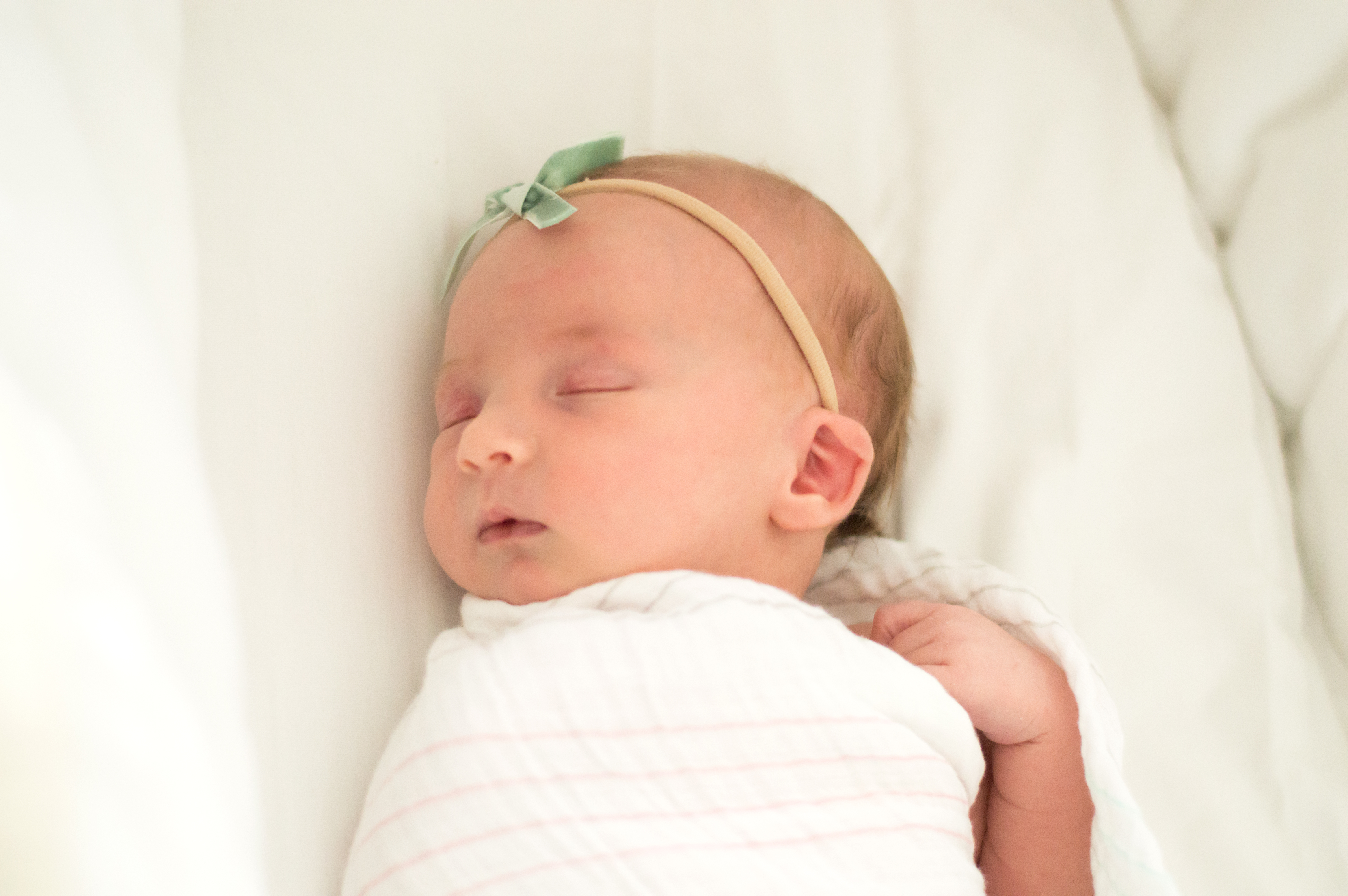 Newborn baby girl in green bow sleeping in bassinet.